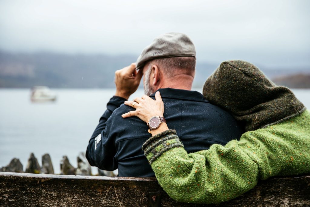 An older couple sits with arms around each other