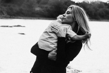 Black and white photo showing a mom lovingly holding her toddler against a scenic lake backdrop. Toddlers are tough, but they are also tender. We can help our children to not feel abandoned