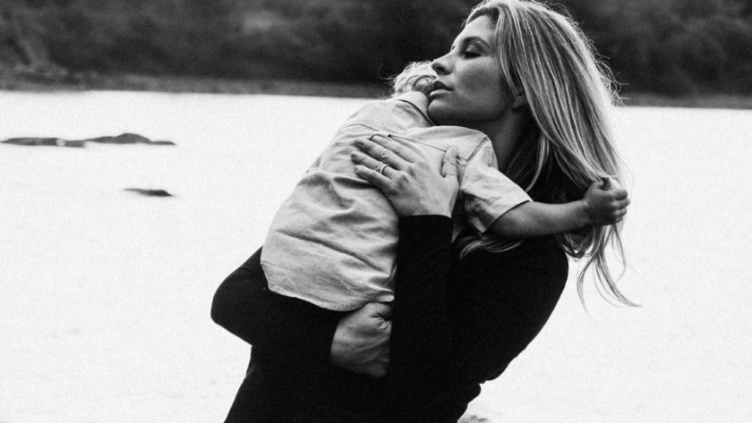 Black and white photo showing a mom lovingly holding her toddler against a scenic lake backdrop. Toddlers are tough, but they are also tender. We can help our children to not feel abandoned