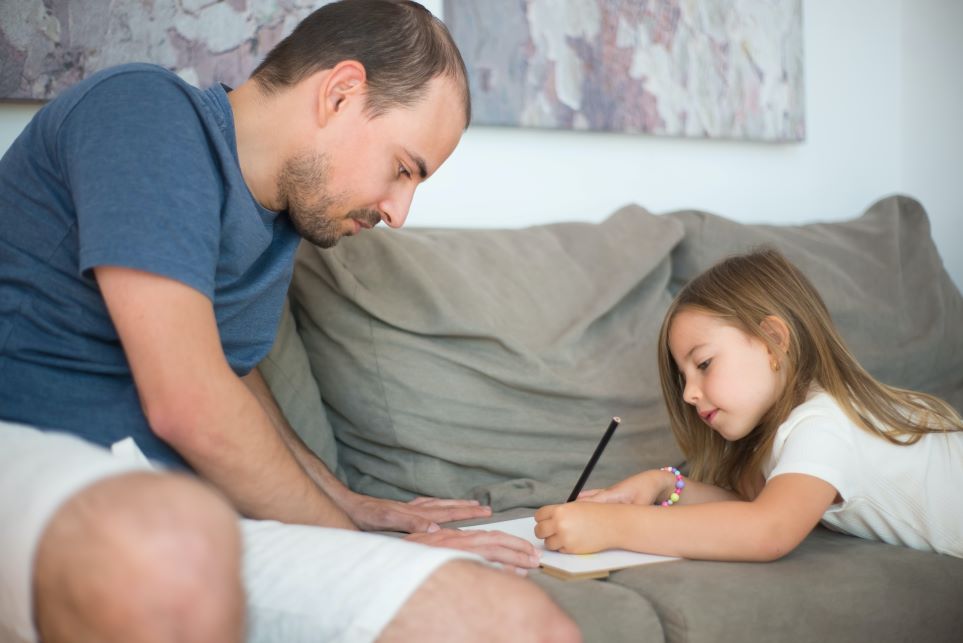 Dad helping daughter use pencil
