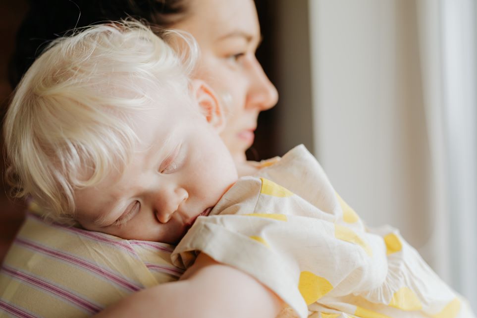 Tired mom holding sleeping baby: parenting at a challenging time