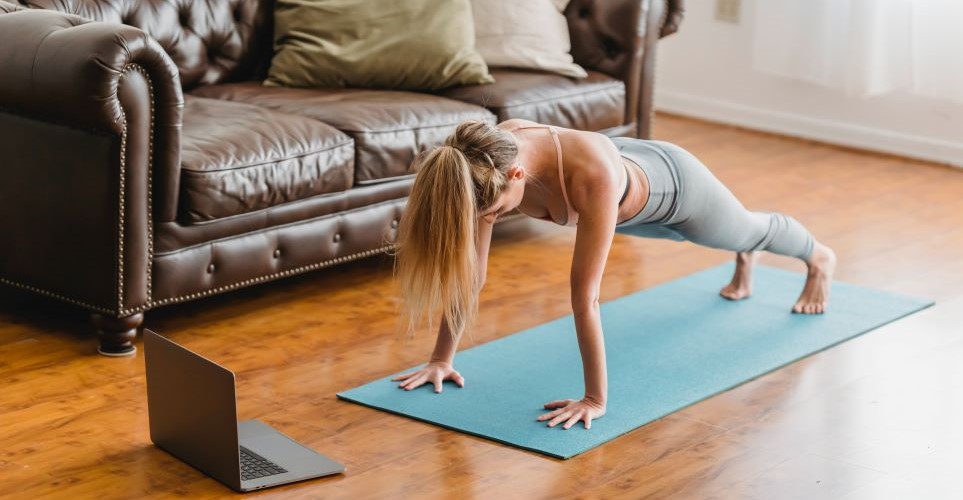 Woman doing plank workout in her home with laptop
