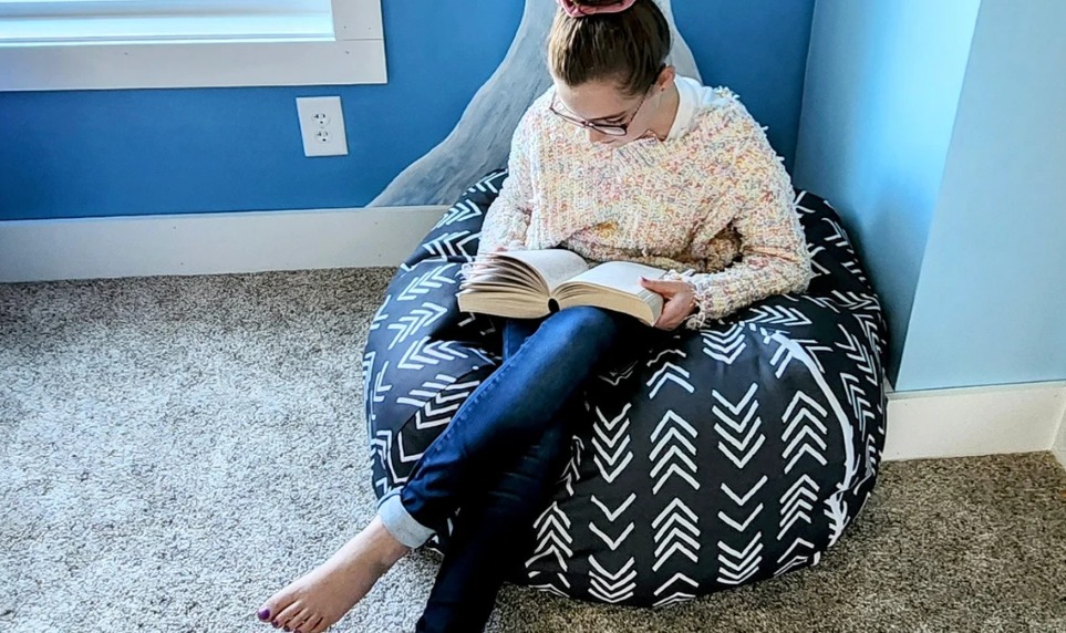 Black plush toy storage beanbag with white chevron design, and girl sitting on it while reading a book