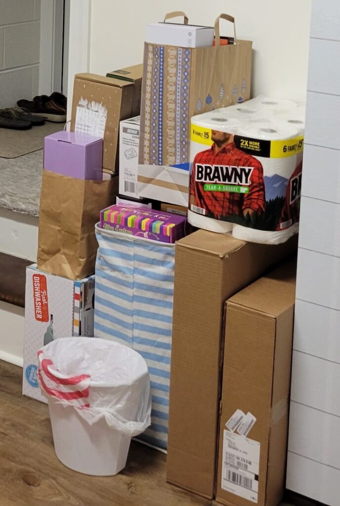 A corner cluttered with stacked cardboard boxes of various sizes and a package of paper towels