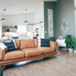 The main living space of a home with an ideal stuff/space ratio: two couches spaced apart in main area, several houseplants lining walls and corners with ample natural light, several throw pillows on couches, small end tables by walls with a few items, and plenty of decor throughout nearby kitchen and on walls