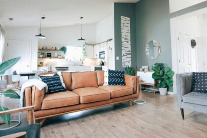 The main living space of a home with an ideal stuff/space ratio: two couches spaced apart in main area, several houseplants lining walls and corners with ample natural light, several throw pillows on couches, small end tables by walls with a few items, and plenty of decor throughout nearby kitchen and on walls