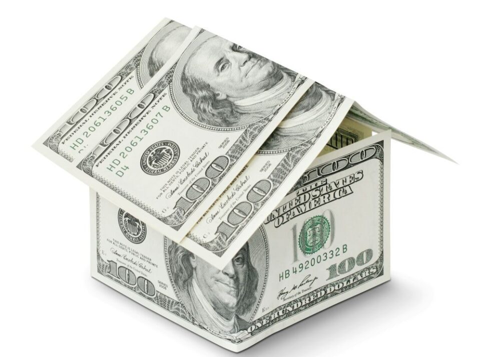 Four one-hundred dollar bills are folded and stacked in the shape of a miniature house, indicating the significant cost buying a new house can entail