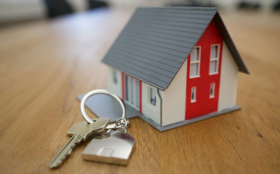 A miniature house rests on a table next to a new house key
