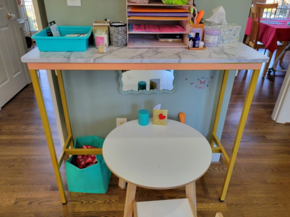 Balance the stuff/space ratio with a tall and narrow console table like the one seen in this photo that leaves minimal furniture footprint. Underneath is a toddler table. On top is a tiered shelf with folders and papers, a bin with miscellaneous items, smaller containers with other miscellaneous items kept out of sight, and a tissue box and other everyday essentials.