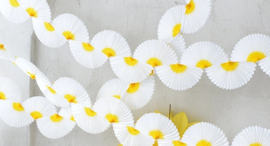 White paper half-fans with yellow centers strung as a garland span the page against a white stucco wall