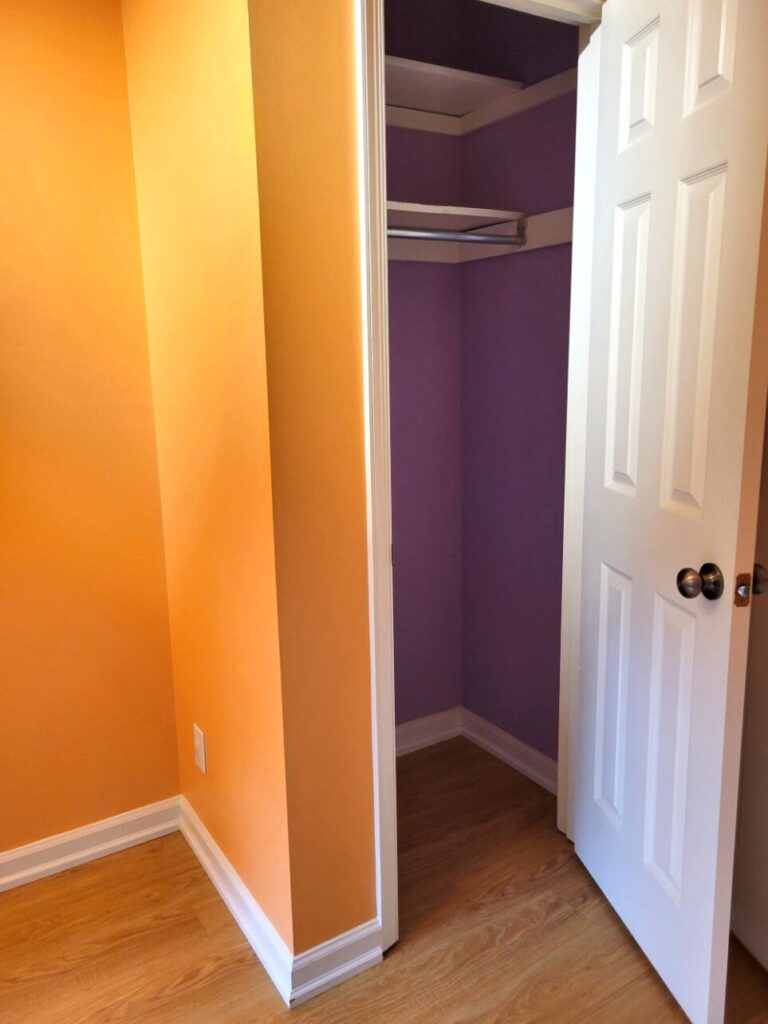 View of coat closet in front entryway at old house. The front entryway's walls are painted a light peach/orange, and the inside of the open coat closet is painted periwinkle