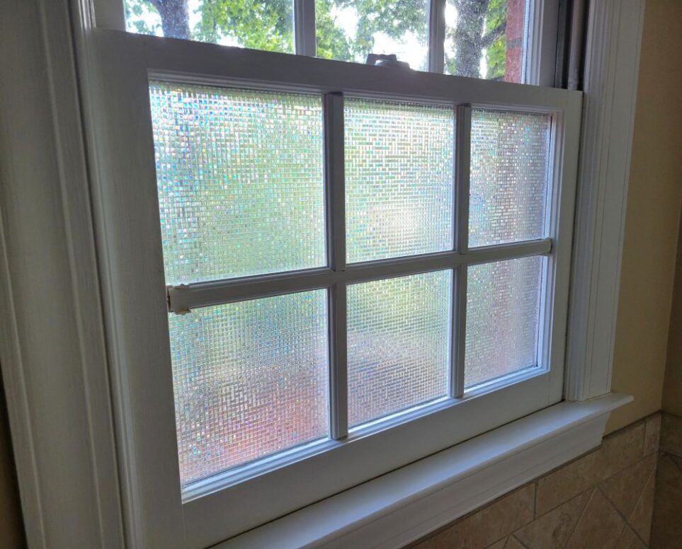 One of the two square-shaped primary bathroom windows, which (along with all windows in this house) is divided into smaller sections by removable white-painted wooden 'window pane dividers'. The lower six sections, seen up-close in the photo, are covered in a stick-on iridescent/clear film to give privacy whilst still letting in natural light. In the above three sections (barely seen in photo - mostly out of shot), the glass is bare so treetops are still seen unobscured yet high enough for privacy from houses behind