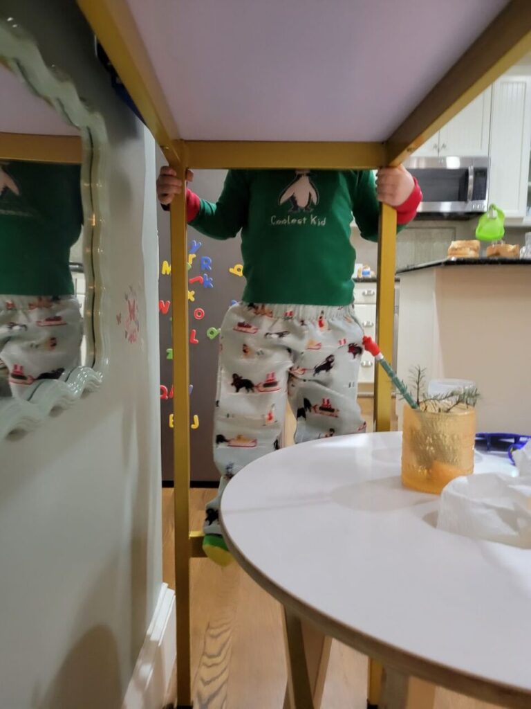 Console table viewed from below, with toddler standing on lower crossbar supporting legs (to reach above the top). Also partially underneath is his toddler table