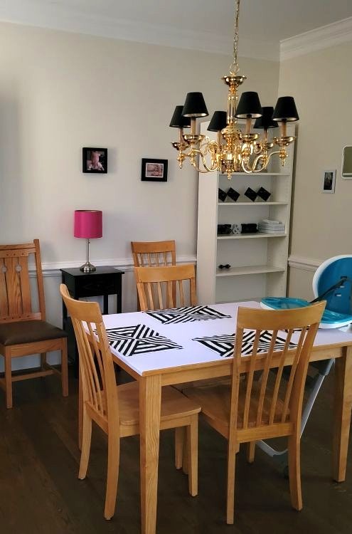 Dining room table and chairs situated below gold-coloured candelabra-style chandelier with small black lampshades. The light fixture provides a dim light but not, being overhead, doesn't amply light the entire space