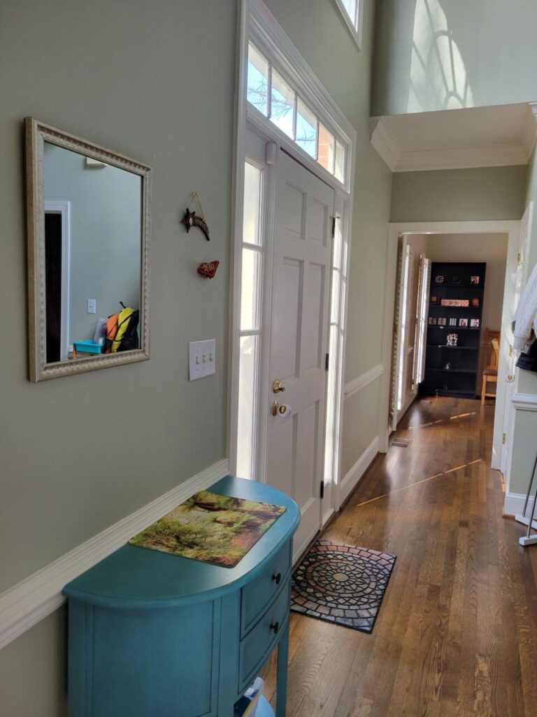 View of foyer from side (front living room) showing blue table below mirror, just next to front door. In far view ahead is dining room seen through doorway.