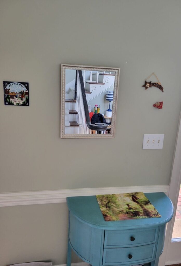 The blue table just inside front door in foyer, at bottom of stairs, serves as a catch-all to set things coming in and out of the house. Hanging on the wall above it is a mirror and on either side a couple of small wall decorations