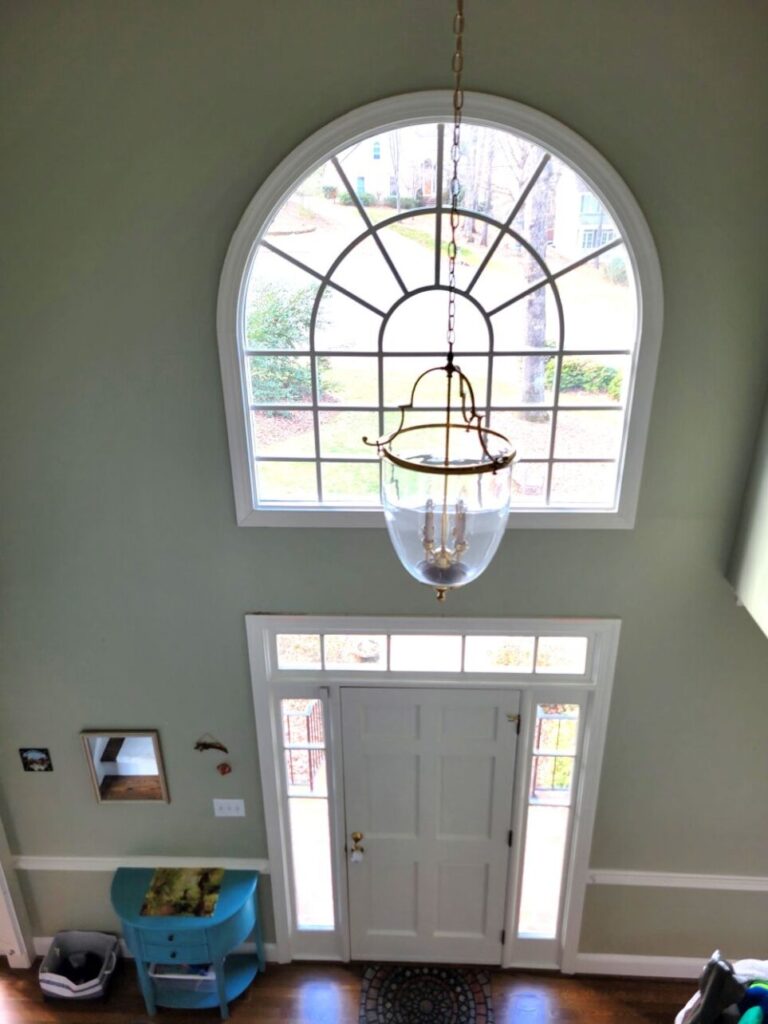 The front door and lunette window above it as seen from second floor hallway looking over stair rail