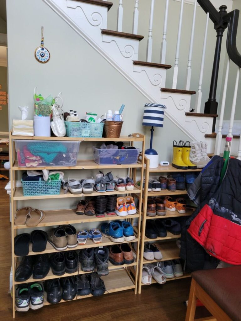 For a manageable stuff/space ratio, neatly consolidate shoes on shoe racks as seen in this photo of two tall shoe racks lined up under the stairwell with organized storage bins on the top for everyday-use items