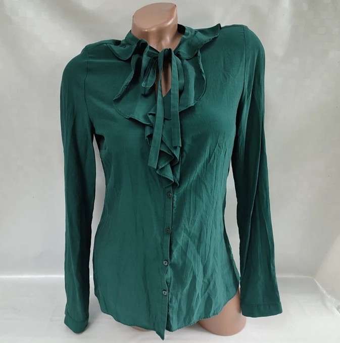 A mannequin bust wears an emerald green jabot-style blouse