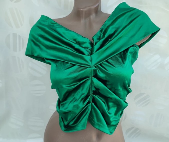 A mannequin bust wears a silky emerald green cap-sleeve crop top with bunched/gathered fabric