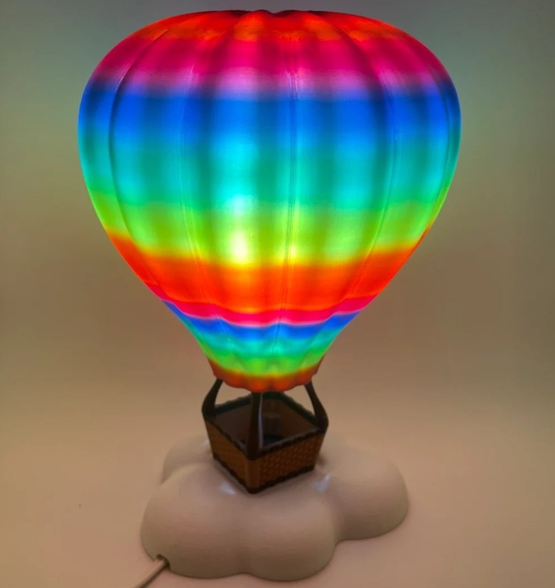 A plastic 3D-printed hot air balloon lamp in ombre rainbow stripes glows from its bulb inside