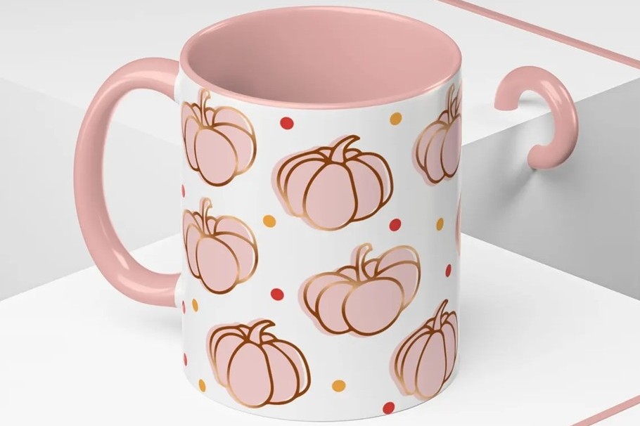 Close-up photo of a white mug with a pink interior and pink handle with pink pumpkins on it