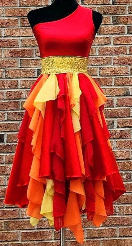 An asymmetrical sleeveless flowy flame-coloured dress on a mannequin features a calf-length skirt with flowing layers of fabric in red, orange and yellow, a sparkly gold sash, and a vivid shiny red top going over one shoulder, a beautiful dress for classy Halloween costumes featuring fire and flames