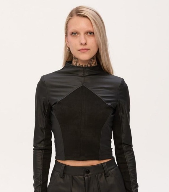 A model with long blonde hair stands wearing a long-sleeved fake leather and velvet black shirt