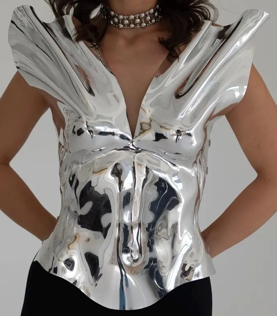 A woman models a shiny silver metallic sculpted corset that flairs at the shoulders. It's not only actually wearable but makes for fantastic eccentric decor