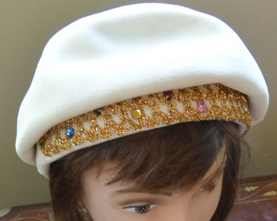 Close-up photo of a white Schiaparelli hat on a mannequin head, with a gold-embroidered brim with different coloured sequins