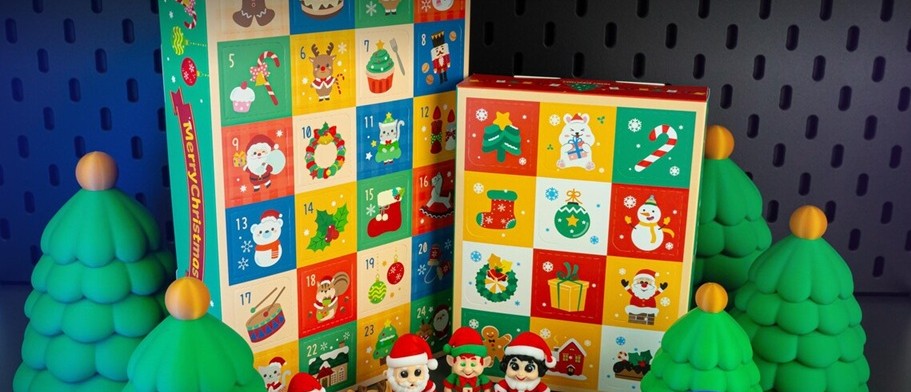 A box of the regular size and mini-size fidget toy advent calendars, with a few of the fidget figures shown standing at the base of the box - an elf, Santa, etc.