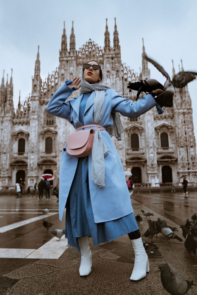 Model (@marwaatik) posing in a sky blue dress and jacket with white boots at the Duomo in Milan, Italy during Milan Fashion week February 2018