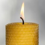 Close-up photo of the top of a lit beeswax candle in the traditional honeycomb-indented 'rolled' pillar shape. Beeswax candles like these are some of the best clean burning candles