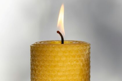 Close-up photo of the top of a lit beeswax candle in the traditional honeycomb-indented 'rolled' pillar shape. Beeswax candles like these are some of the best clean burning candles
