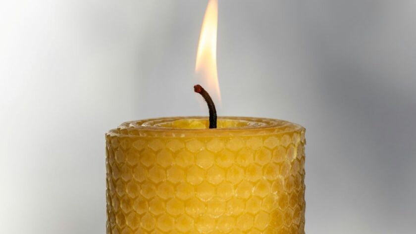 Close-up photo of the top of a lit beeswax candle in the traditional honeycomb-indented 'rolled' pillar shape. Beeswax candles like these are some of the best clean burning candles