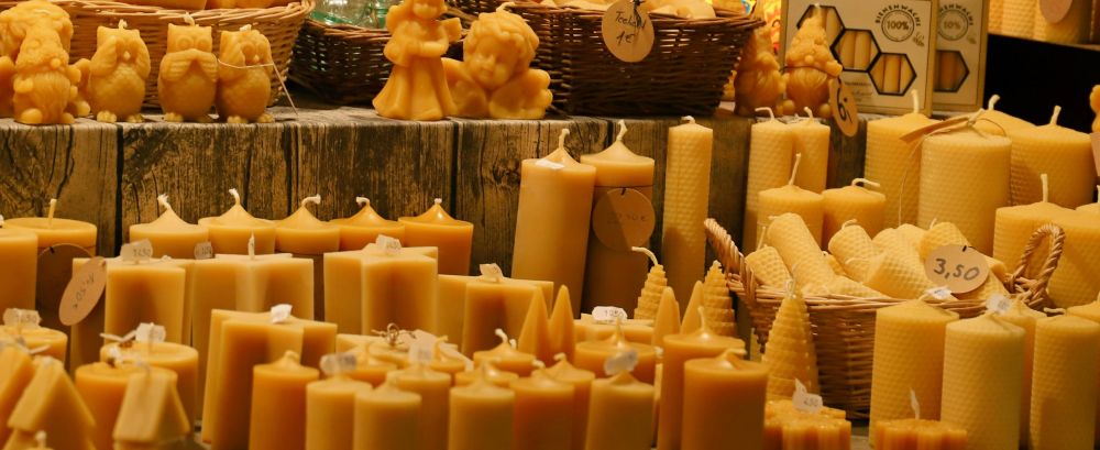 Close-up photo of a beeswax candle seller's stall at the Kassel Christmas Market in Hessen, Deutschland. Beeswax candles in various shapes and sizes including pillars, carved angels, owls, Christmas trees, houses, etc. line the shelves. Beeswax candles are some of the best (and original) clean burning candles and have served as traditional candles for millennia