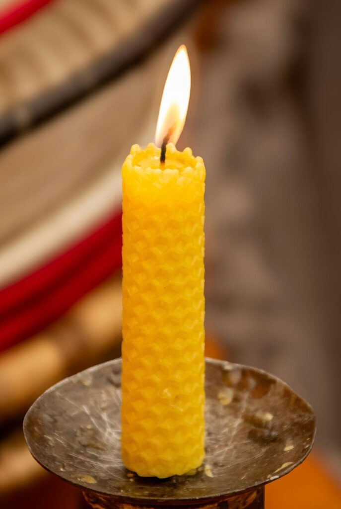 Close-up photo of a narrow beeswax pillar candle lit and atop an old brass candlestick