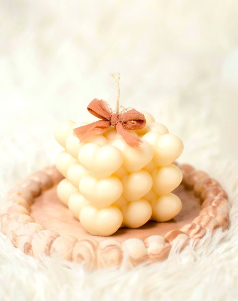 Close-up photo of a cream-coloured candle shaped like a cube composed of many small hearts (three to a row/column) with a small tan bow tied around its wick