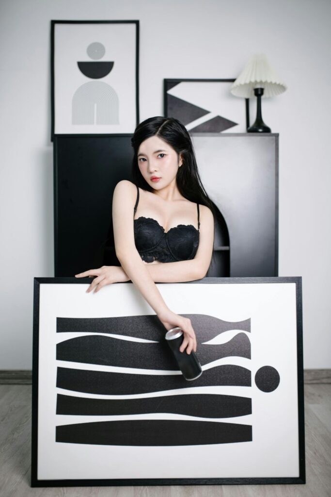 Picture of a model (who suspiciously resembles Ningning from aespa) posing behind a black framed black and white abstract art print