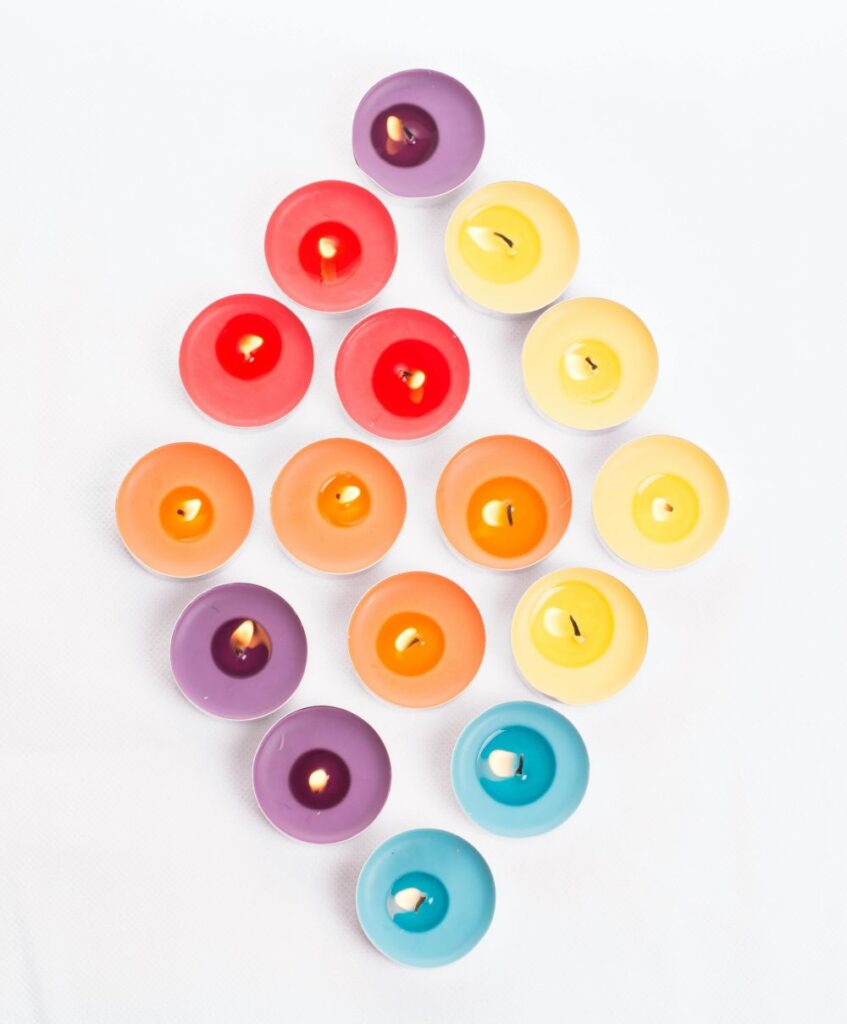 An bright array of several lit tealights of various colours (red, purple, yellow and blue) arranged in a diamond-shape pattern