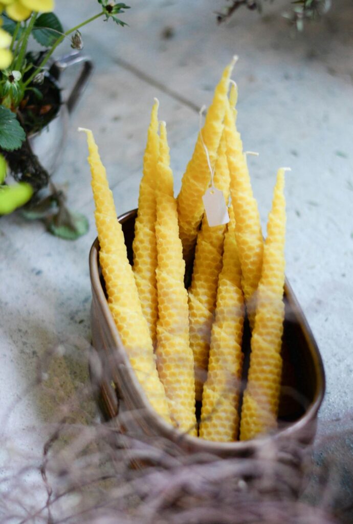 A ovular tin bucket filled with several spiral-rolled beeswax taper candles, traditional clean burning candles