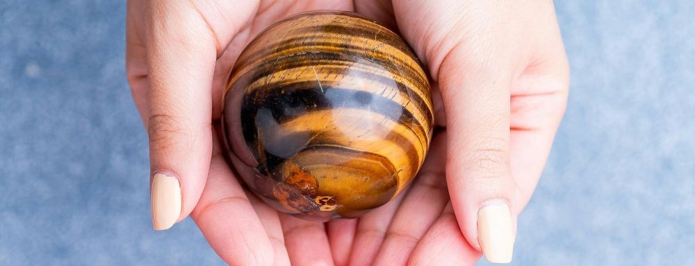Close-up photo of a person holding a tiger's eye sphere in the palm of their hands