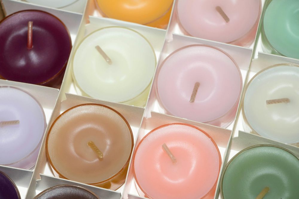 Top-down close-up photo of a box filled with tealight candles in various pastel colours including light pink, off-white, tan, sage green, etc.