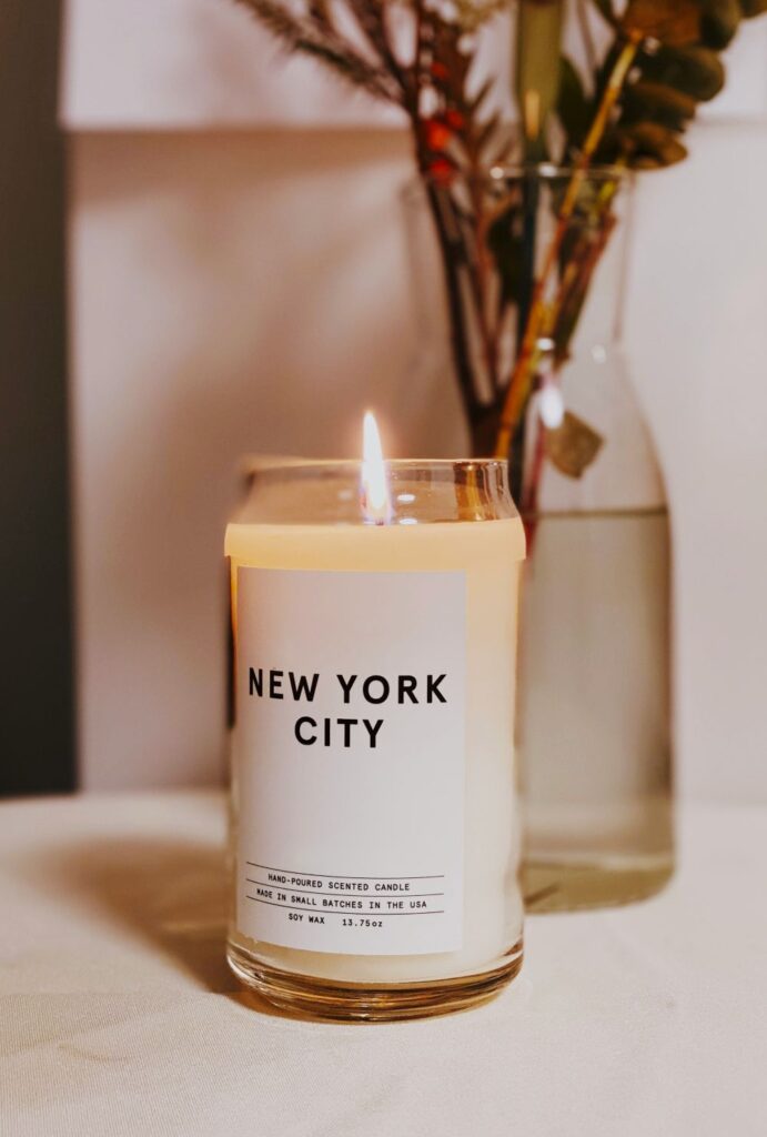 Photo of a lit candle in a clear glass jar with a label that reads 'New York City' and 'hand-poured scented candle made in small batches in the USA, soy wax' - representing one of the many places in the world with small, local businesses creating clean burning candles