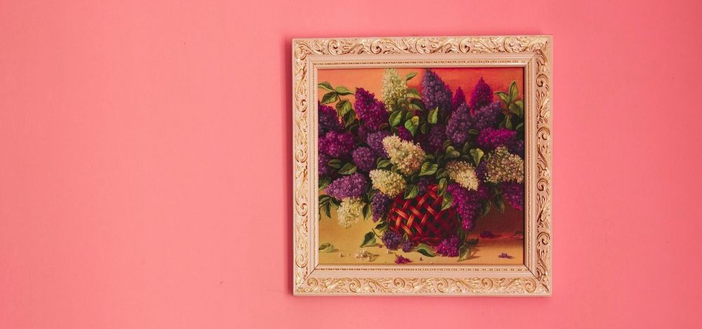 A framed photo of a basket of purple flowers hangs on a pink-coloured wall
