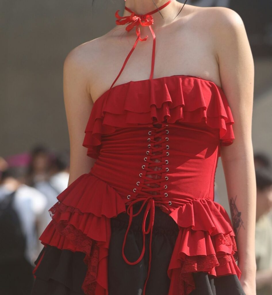 Close-up photo of a woman in a sleeveless red lace-up boddice top with matching choker ribbon and ruffled black skirt, inspiring Babymetal-style classy Halloween costumes