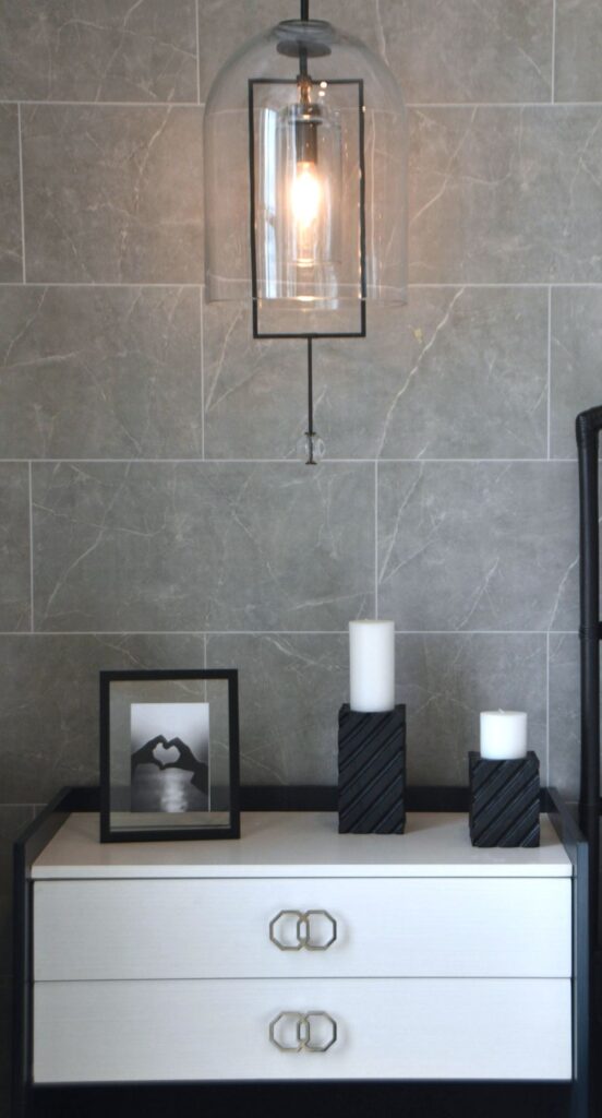 A smart white nightstand in white with black trim beside a (barely in view) black bedframe, with white pillar candles in black rectangular candle holders on top, and a black-framed photo.