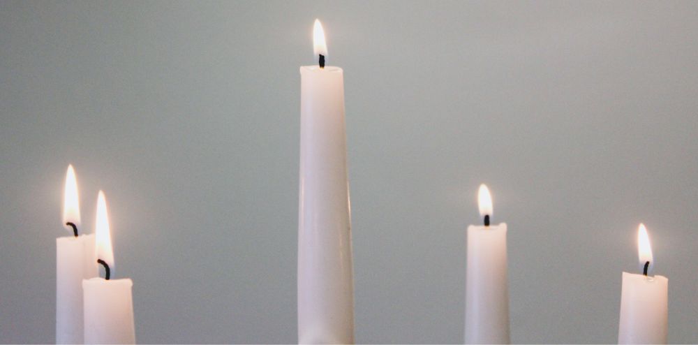 Close-up photo showing the tops of five lit white taper candles