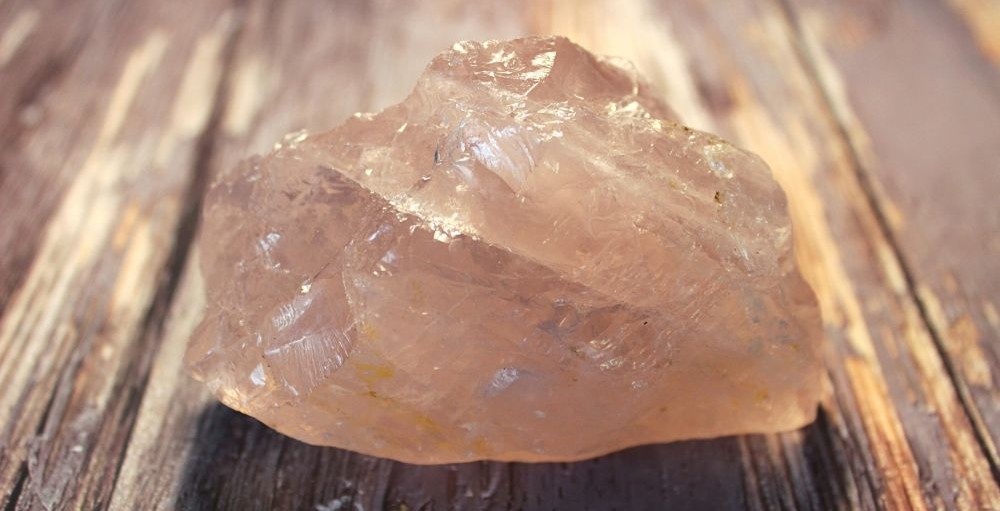 Close-up photo of a raw rose quartz crystal on a wood surface