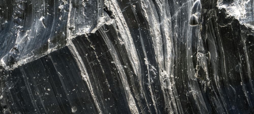 Close-up photo of the surface of raw black obsidian, with white streaks and speckles in it